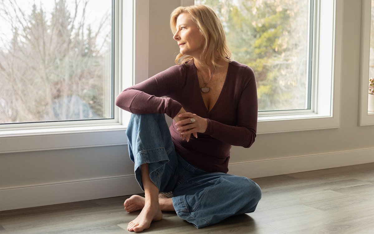 Laura Harvey looking out a window while seated in jeans